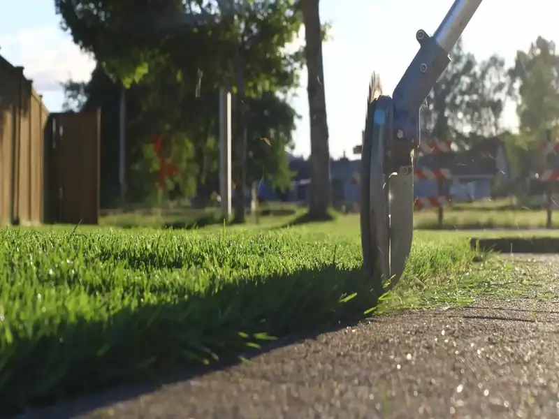 Lawn edger trimming grass along a concrete sidewalk